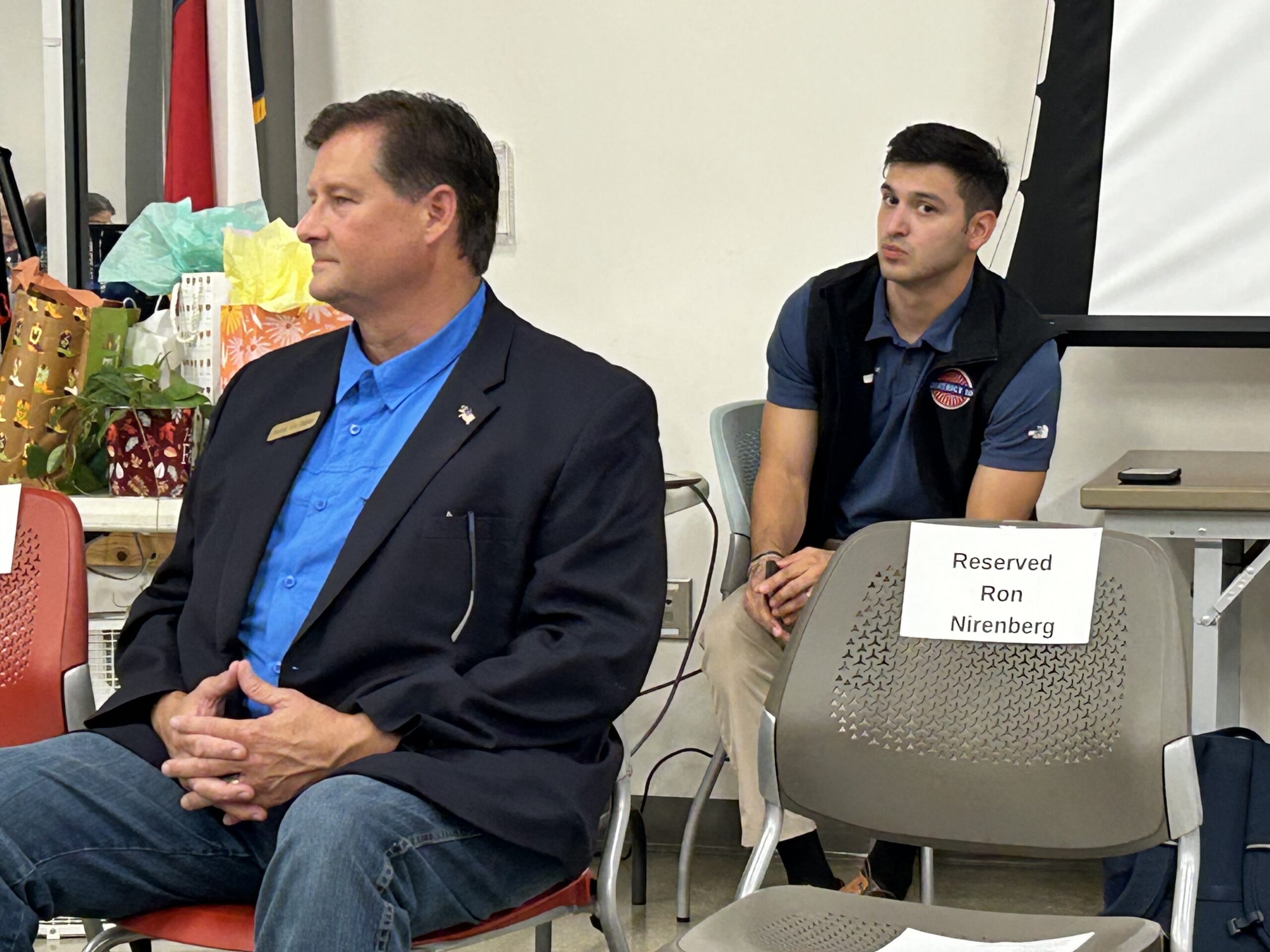 Patrick Von Dohlen seated beside an empty chair bearing a Reserved Ron Nirenberg sign at the October 19 candidate forum.