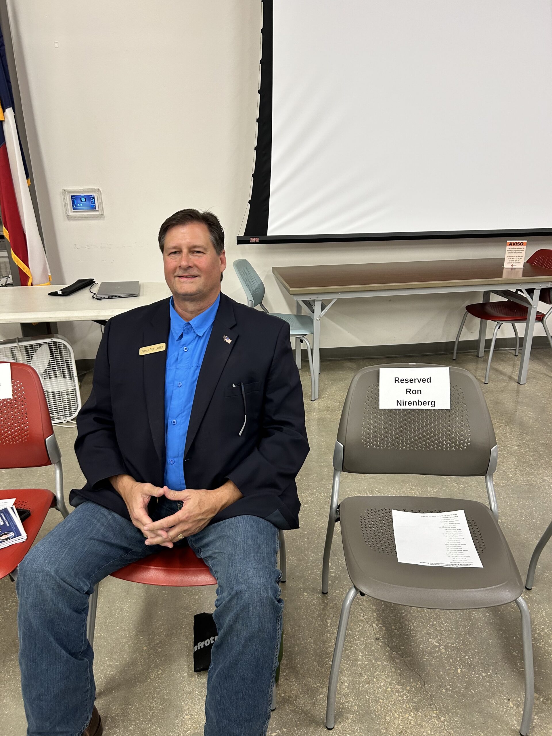Full view of Patrick seated next to the empty chair labeled Reserved Ron Nirenberg.